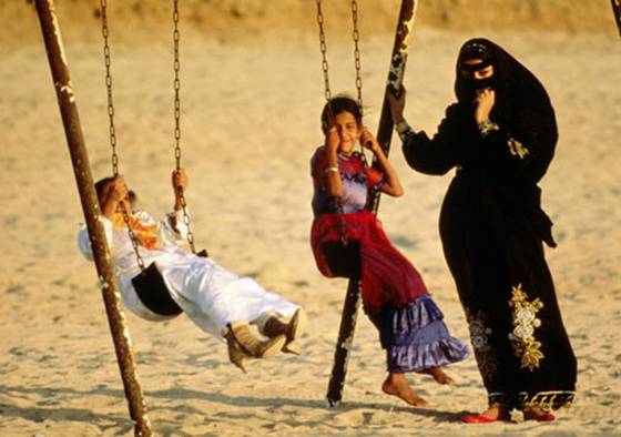 Photo: Veiled mother with children on swings at the beach in Jiddah